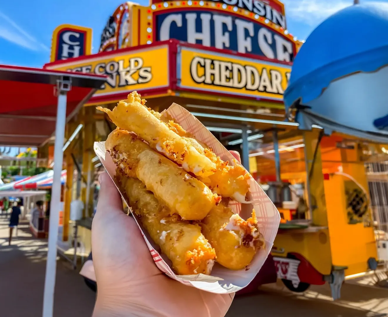 Hand holding mozzarella sticks in front of food vendors at Tiblow Days festival in Bonner Springs Kansas