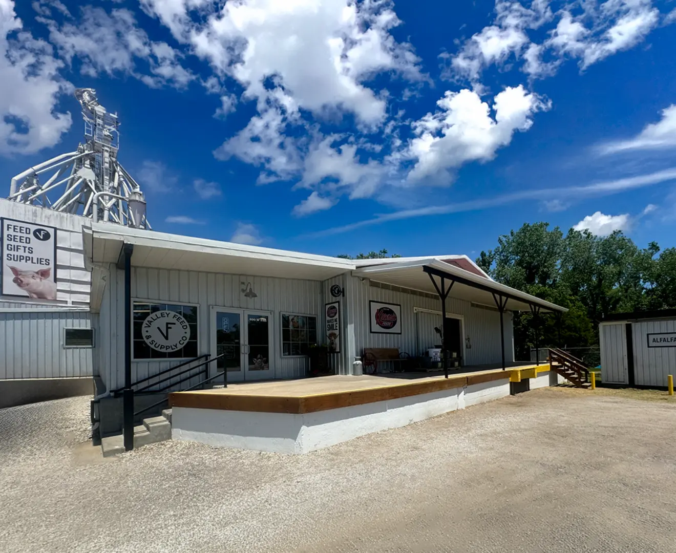 Front entrance of Valley Feed & Supply with the mill visible in the background on a sunny day with clouds.